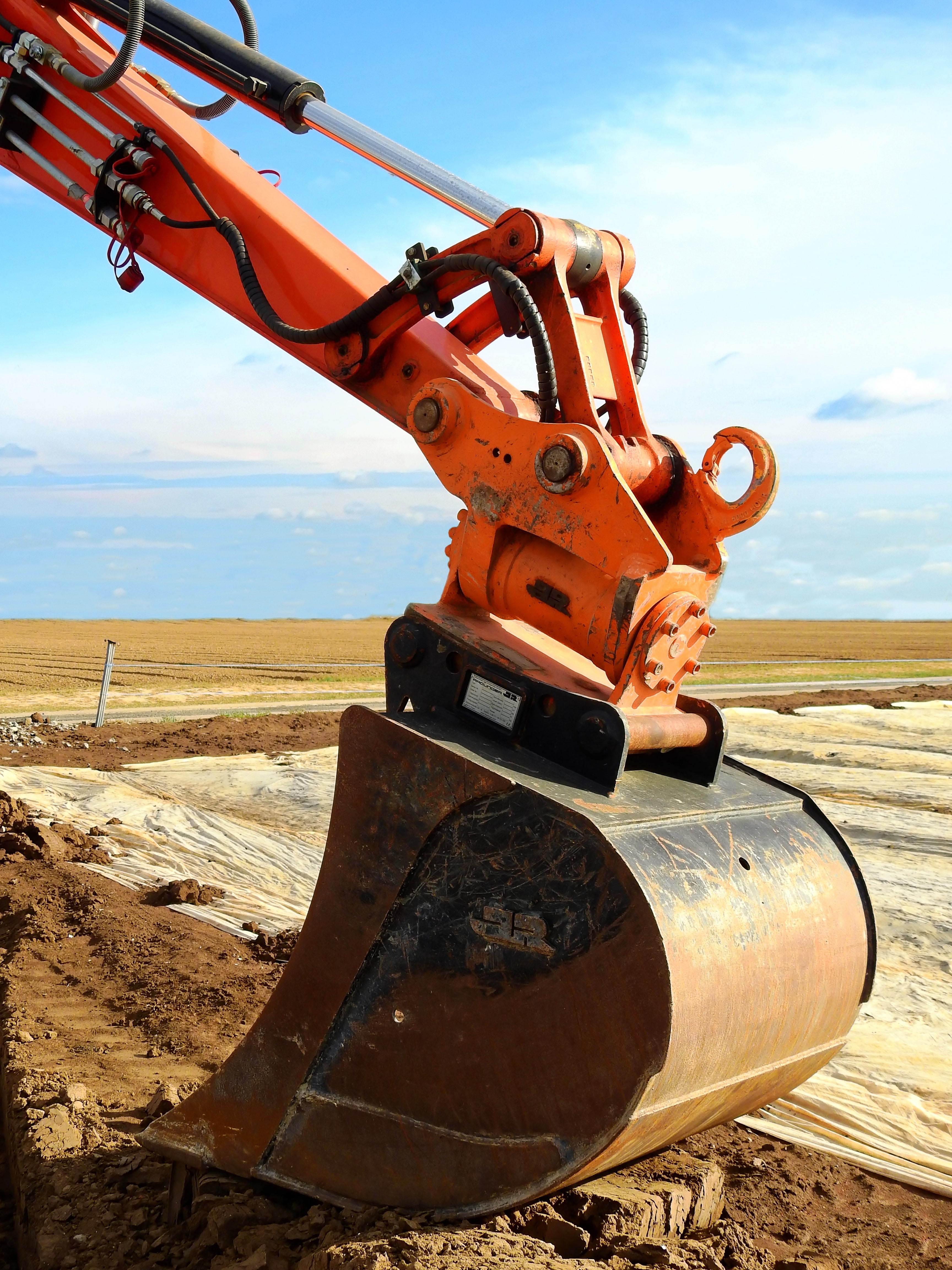 Orange excavator arm digging up red dirt.