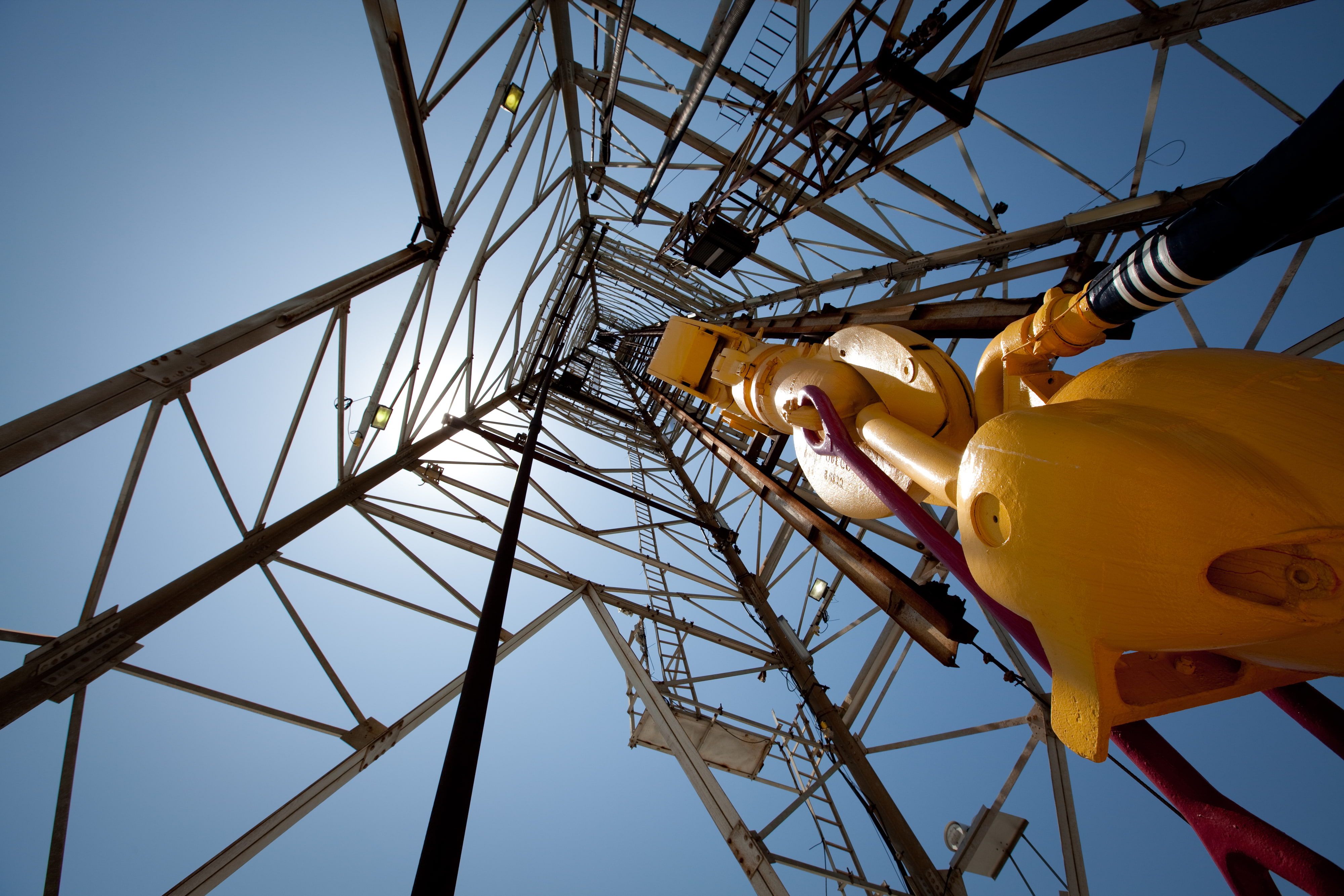 Looking up into an oil rig from the bottom. The oil rig has yellow bars. There is a blue sky in the background