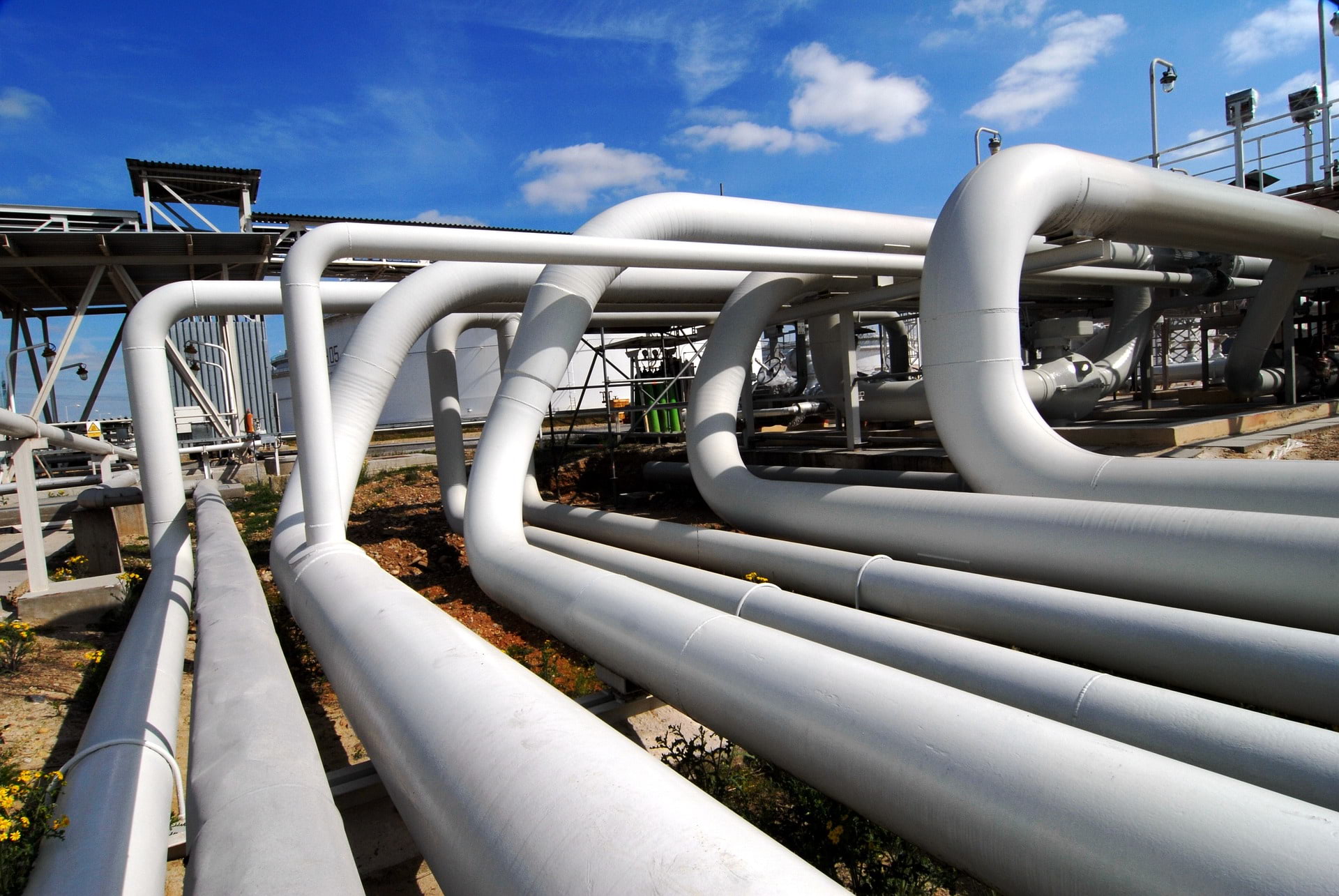 White industrial pipes running horizontally on top of a structure against blue sky.