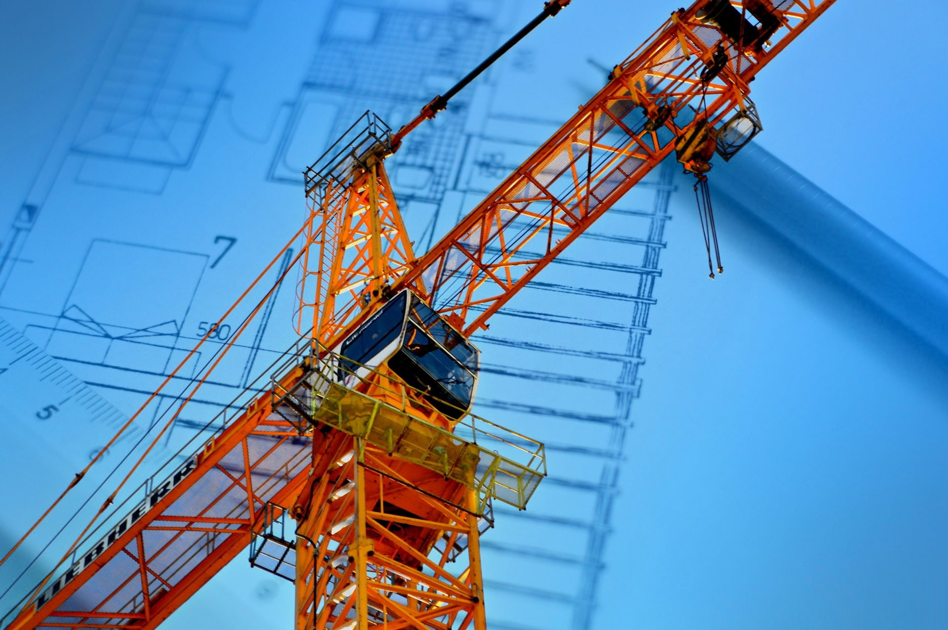 Orange crane against a background of a blueprint of a house with a pen lying on top of the blueprint.